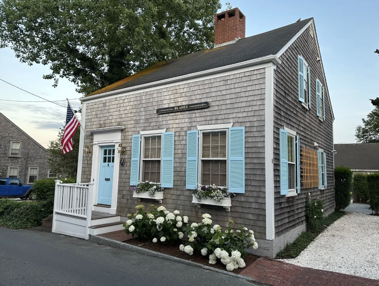 Historic grey shingle Nantucket cottage with blue shutters, hydrangeas, and American flag in the historic district